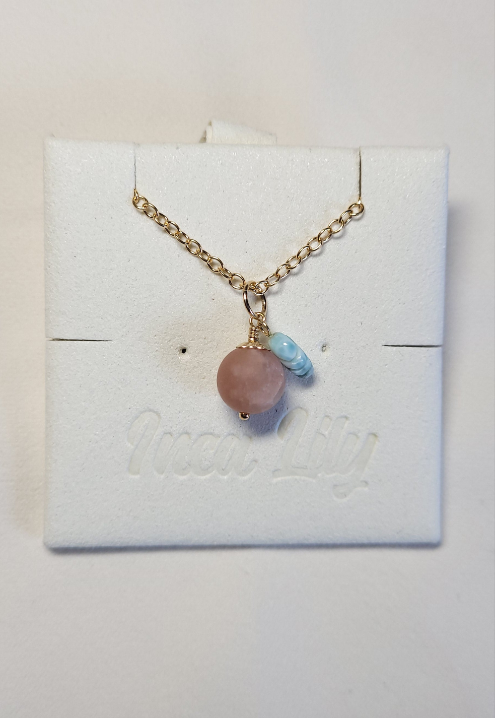 A gold-filled chain necklace with a sunstone berry and carved Larimar leaf pendant