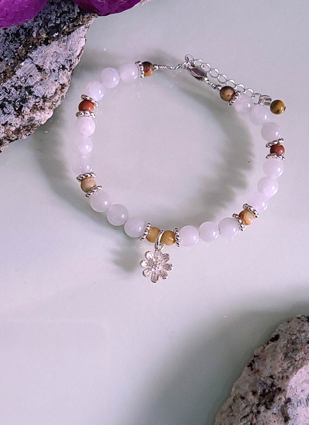 A bracelet with moonstone, crazy lace agate, and silver strung on silver wire adorned with a silver daisy charm.