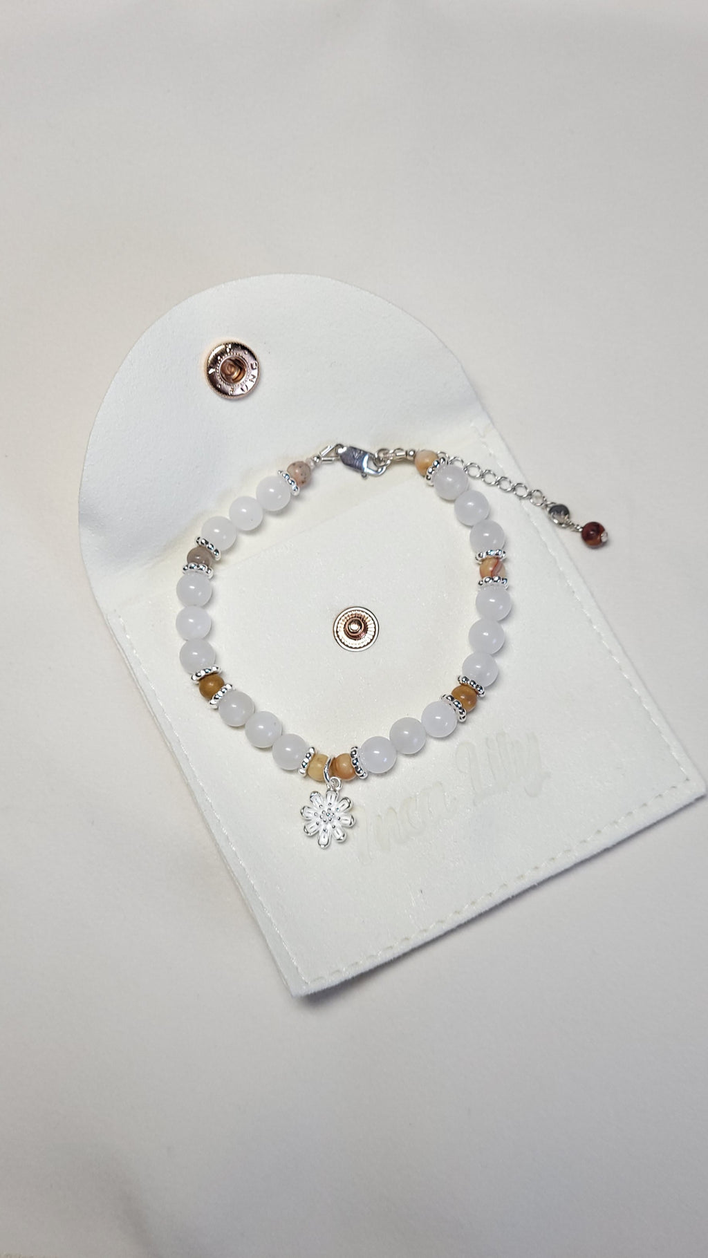 A bracelet with moonstone, crazy lace agate, and silver strung on silver wire adorned with a silver daisy charm.